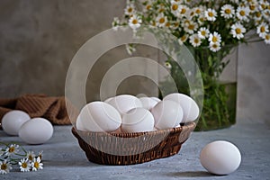 Fresh white eggs in a basket with wildflowers in a vase