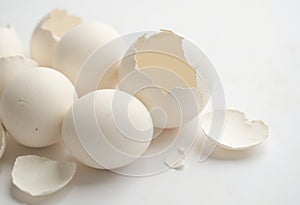 Fresh white eggs with broken shells scattered on a light background