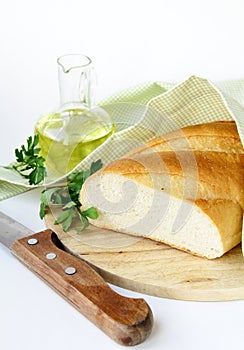 Fresh white loaf of bread with a knife , olive oil