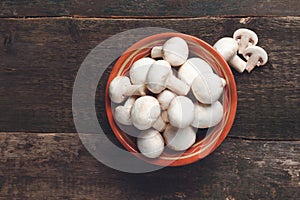 Fresh white mushrooms champignon in brown bowl on wooden background. Top view. Copy space.