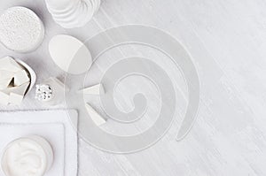 Fresh white natural cosmetics - white cream, soap, salt, towel and bath accessories on soft light white wood table, border.