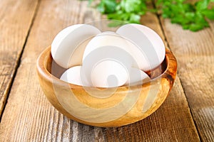 Fresh white raw chicken eggs with parsley on an old wooden table.