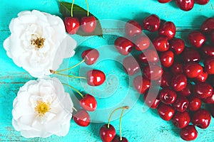 Fresh white roses with water drops, red cherry in a shape of a heart on an old painted wooden table as a bright colorful summer