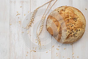 Fresh white round classic wheat bread, wheat ears and grains on white wooden background top view. Bread making, bakery, healthy