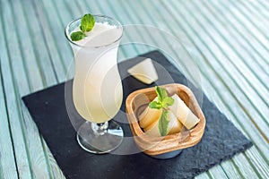 Fresh white smoothie in a glass with sliced pieces of melon and mint on a blue wooden background. Summer cool drinks