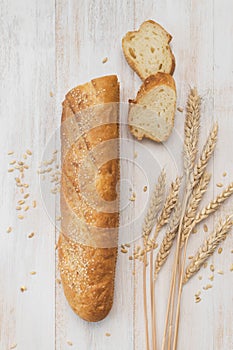 Fresh white wheat bread, french baguette, wheat ears and grains on white wooden background top view. Bread making, bakery, healthy
