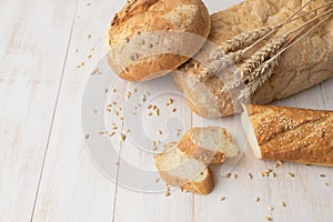 Fresh white wheat bread, round classic, ciabatta, french baguette, wheat ears and grains on white wooden background top view.