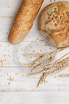 Fresh white wheat bread, round classic, ciabatta, french baguette, wheat ears and grains on white wooden background top view.