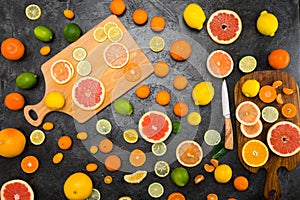 Fresh whole and sliced citrus fruits on cutting boards on black