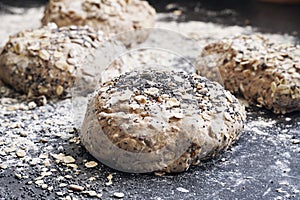 Fresh wholemeal roll, bun dough on table with meal and seeds