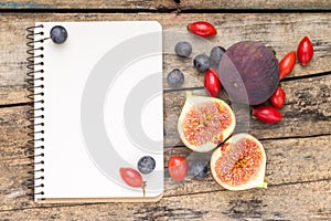 Fresh wild berries and figs with blank notebook on wood background