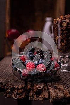 Fresh wild berries in a glass bowl. A variety of fruits and granola. Vertical frame. Rustic style on an old board and a drawer