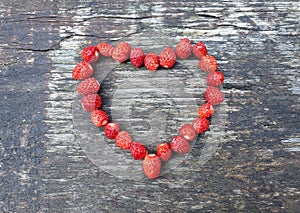 Fresh wild strawberries in shape of heart on wood