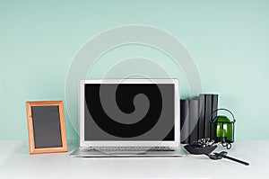 Fresh workplace for education, work with blank notebook screen, black stationery, books, candlestick, photo frame in green mint.