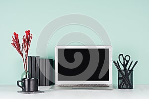 Fresh workplace for education, work with blank notebook screen, black stationery, books, coffee cup, red decoration twig in green.
