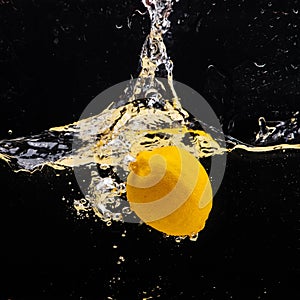 Fresh yellow lemon falling into the water with a splash of water and air bubbles, isolated on a black background