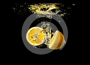 Fresh yellow lemon halves in water splash on black background with lots of air bubbles