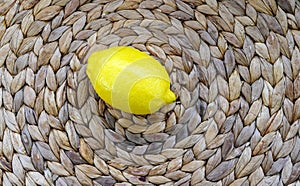 A fresh yellow lemon lies in the center of a natural rattan surface in a country house, ready to eat.