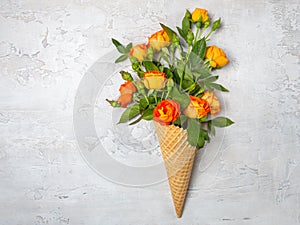 Fresh yellow-orange roses in a waffle cone on a white concrete background. Flat lay. Original packaging of the bouquet