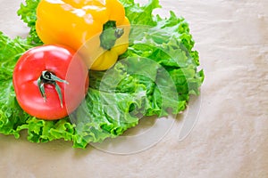 Fresh yellow paprika, tomatoes and green salad leaves on a grey background. Space for text. Healthy eating concept.