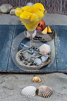 Fresh yellow peach ice-cream scoops in glass cone on the beach,