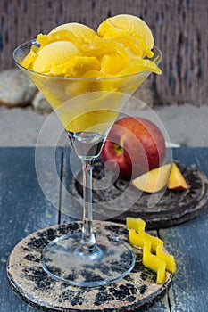 Fresh yellow peach ice-cream scoops in glass cone on the beach,