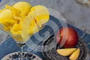 Fresh yellow peach ice-cream scoops in glass cone on the beach,