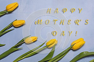 Fresh yellow tulip flowers and mother greeting text on blue concrete