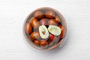 Fresh Ziziphus jujuba fruits in bowl on white wooden table, top view