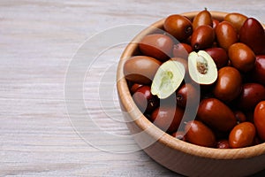 Fresh Ziziphus jujuba fruits in bowl on wooden table, closeup. Space for text