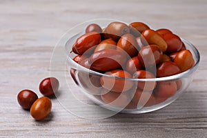 Fresh Ziziphus jujuba fruits with glass bowl on wooden table, closeup