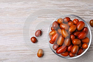 Fresh Ziziphus jujuba fruits with glass bowl on wooden table, flat lay. Space for text