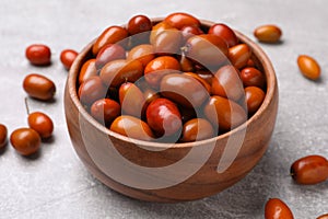 Fresh Ziziphus jujuba fruits in wooden bowl on light table, closeup