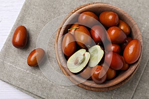 Fresh Ziziphus jujuba fruits with wooden bowl and napkin on table, flat lay