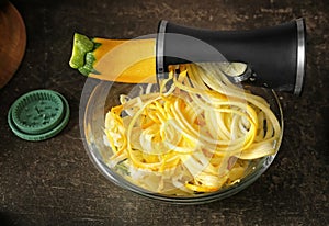 Fresh zucchini spaghetti in bowl with spiral grater on dark table