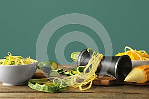 Fresh zucchini spaghetti with spiral grater on wooden table against color background