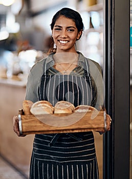 The fresher the better. a young woman holding a selection of freshly baked breads in her bakery.