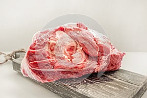 The freshest beef knuckle with bone lies on a wooden thick board on a light background. Close-up. Copy space photo
