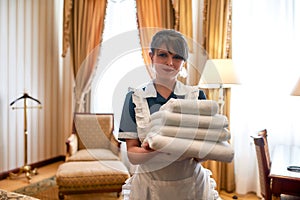 Only the freshest. Hotel maid in uniform smiling while holding stack of clean white towels for guests while cleaning and