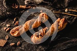 Freshly backed twisted cakes or puff pastry buns with chocolate on rustic sackcloth background. Pastries and bakery, close up