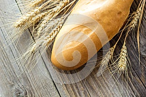 Freshly baguettes baked bread and wheat spikes on wooden background