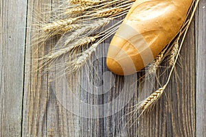 Freshly baguettes baked bread and wheat spikes on wooden background