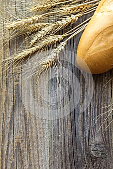 Freshly baguettes baked bread and wheat spikes on wooden background