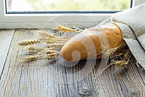 Freshly baguettes baked bread and wheat spikes on wooden background