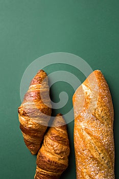 Freshly baked artisan croissants whole baguette with golden crust floury on dark green background. Top view. Minimalist modern