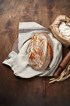 Freshly baked Artisan sourdough bread loaves with wheat spike and bag of flour on dark wooden background