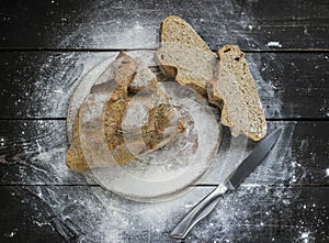 Freshly baked bread with flour and knife on a rustic wooden desk