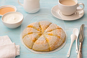 Freshly baked carrot scones with cream, honey and cup of tea with milk on light blue background