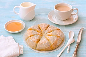 Freshly baked carrot scones with cream, honey and cup of tea with milk on light blue background