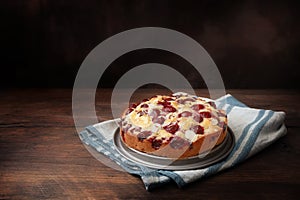 Freshly baked cherry cake with almond slivers on a blue kitchen towel and dark rustic wood, large copy space